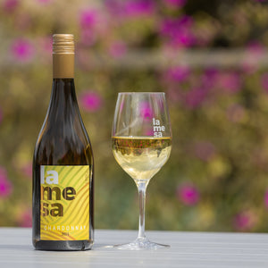 Bottle and glass of La Mesa Chardonnay 2025 white wine with a blurred floral background