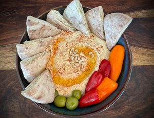 Hummus with pita bread, olives, and peppers on a wooden surface